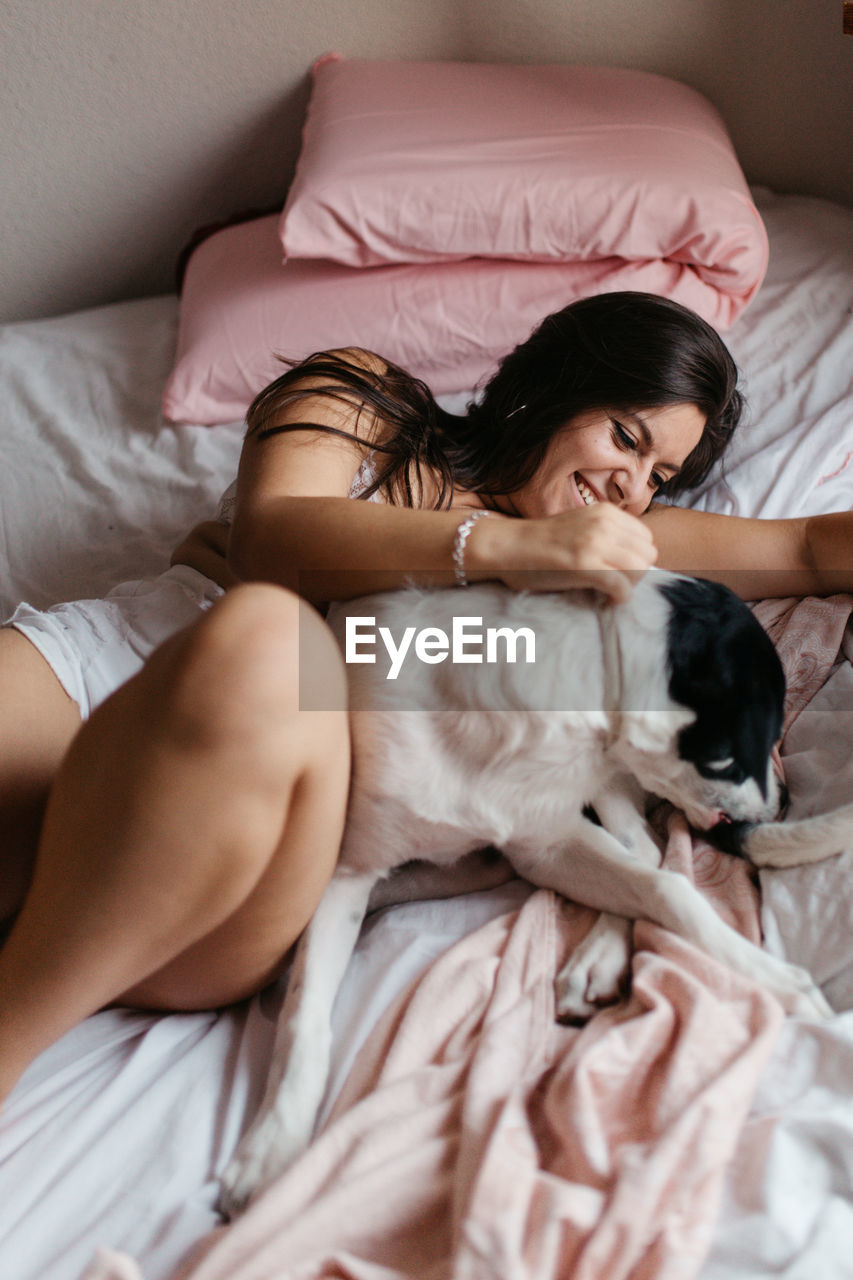 Smiling woman lying with dog on bed