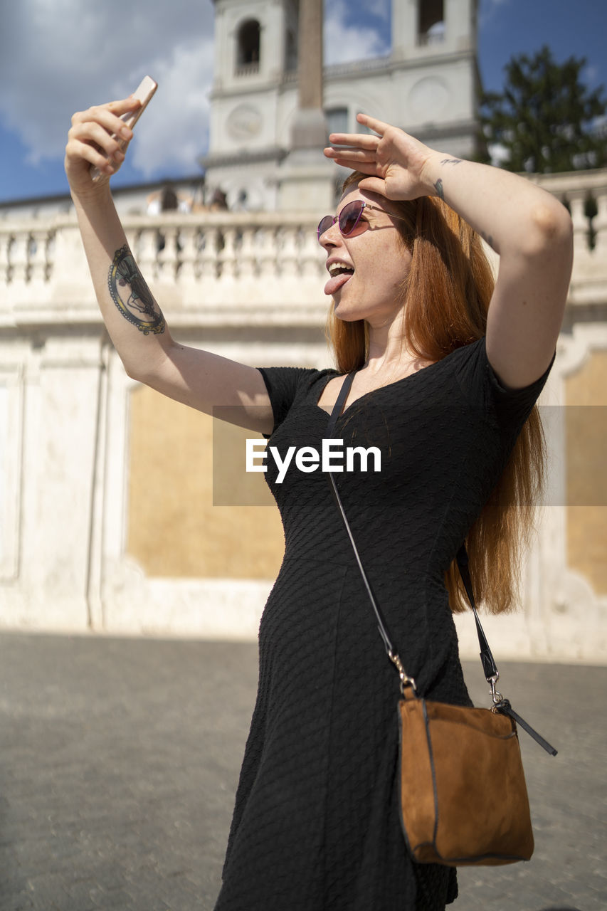 Fashion red hair girl look at phone making funny faces outdoors