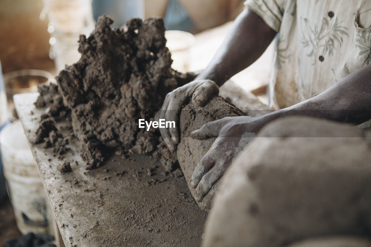 Midsection of worker kneading clay at table in workshop