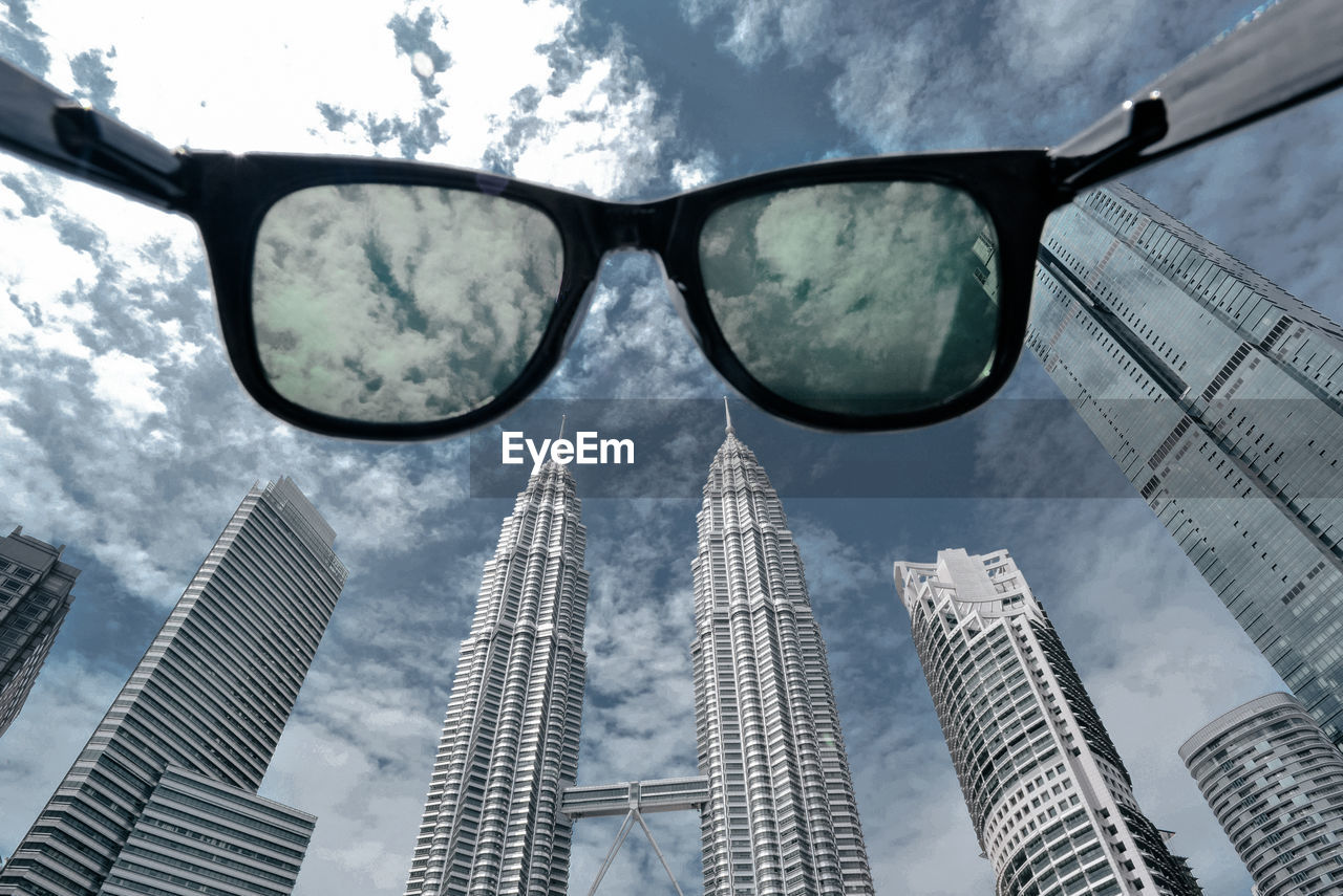 Low angle view of sun glasses facing the modern buildings against bright sky