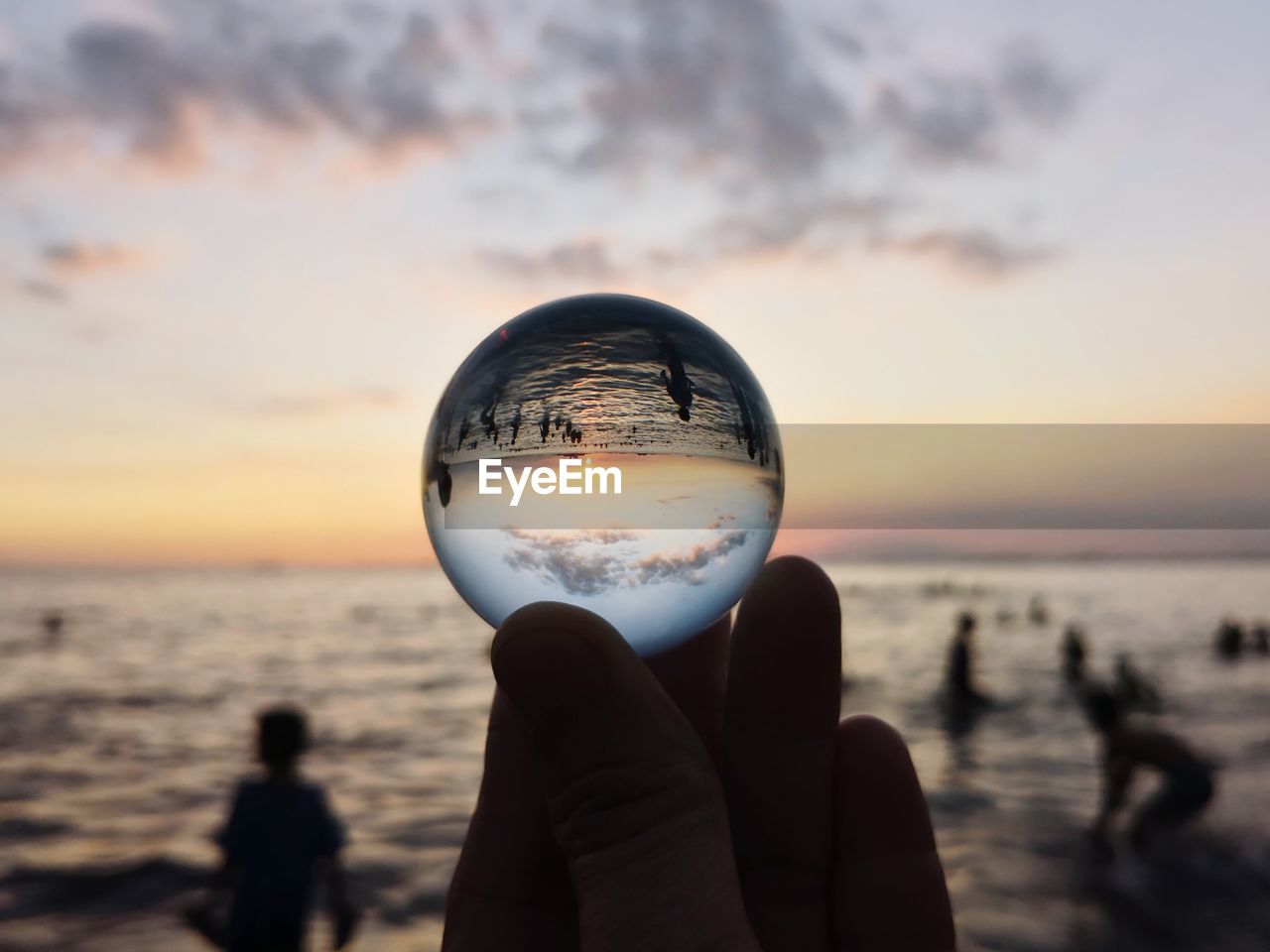 Close-up of hand holding crystal ball against sea and sky during sunset