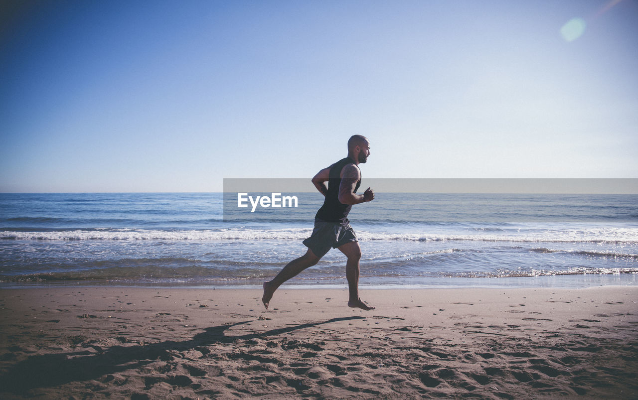 Side view of man running at beach against sky