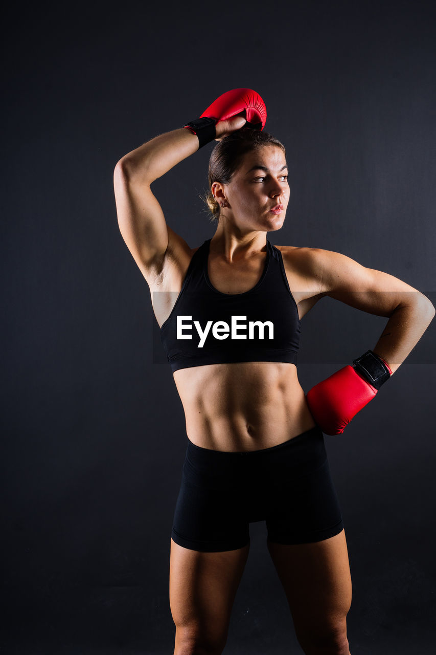 portrait of young woman exercising in gym against black background