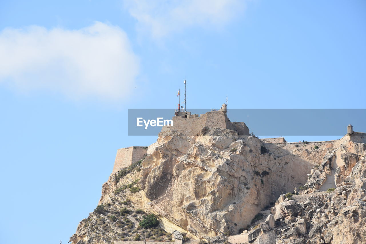 Low angle view of flag on rock against blue sky