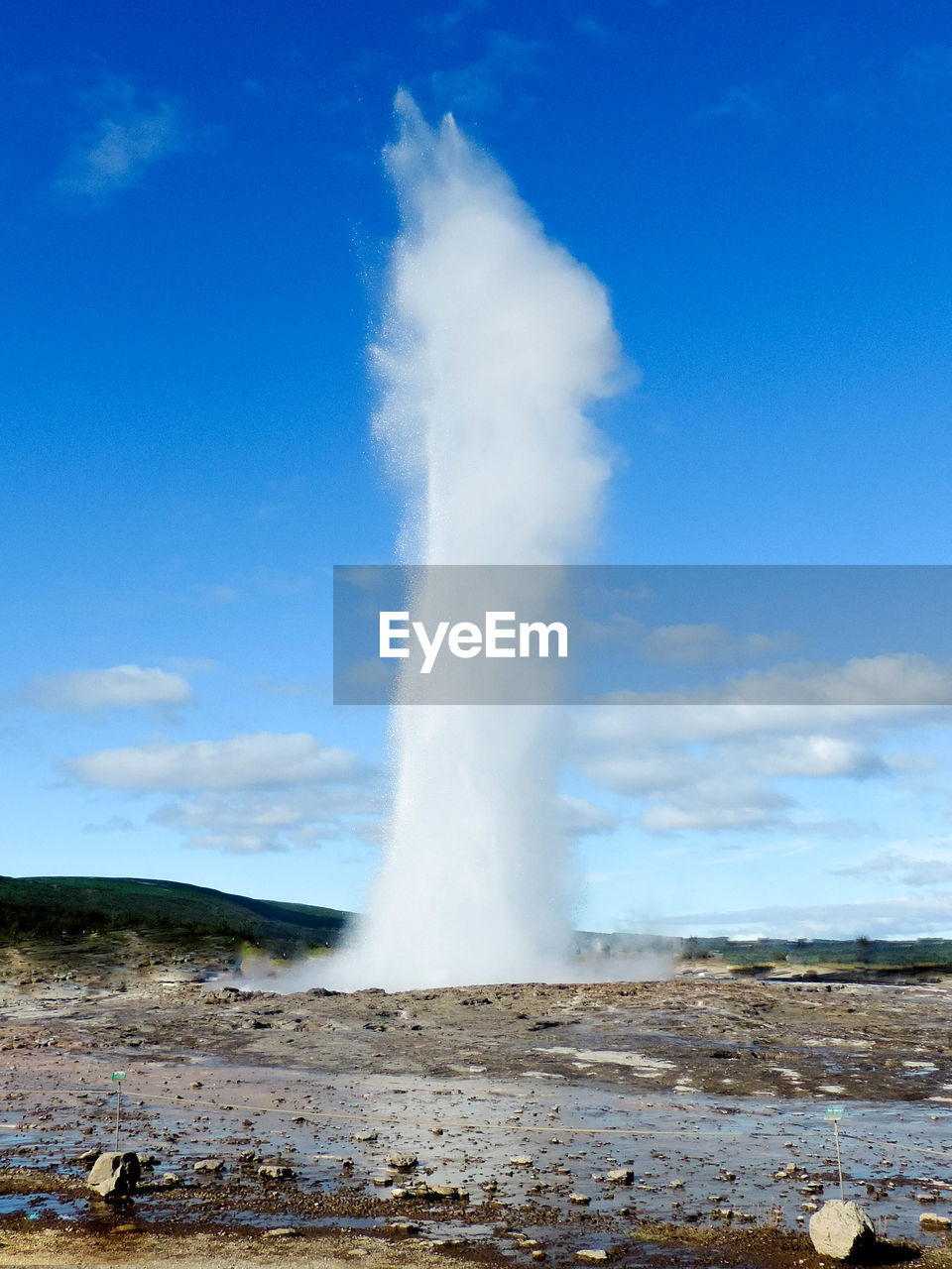 Idyllic view of geyser erupting against blue sky