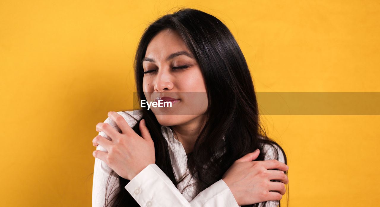 one person, women, adult, yellow, colored background, portrait, person, long hair, young adult, yellow background, female, studio shot, copy space, hairstyle, teenager, indoors, emotion, photo shoot, headshot, lifestyles, smiling, black hair, human face, looking, happiness, holding, clothing, hand, technology, close-up, front view, singing, casual clothing