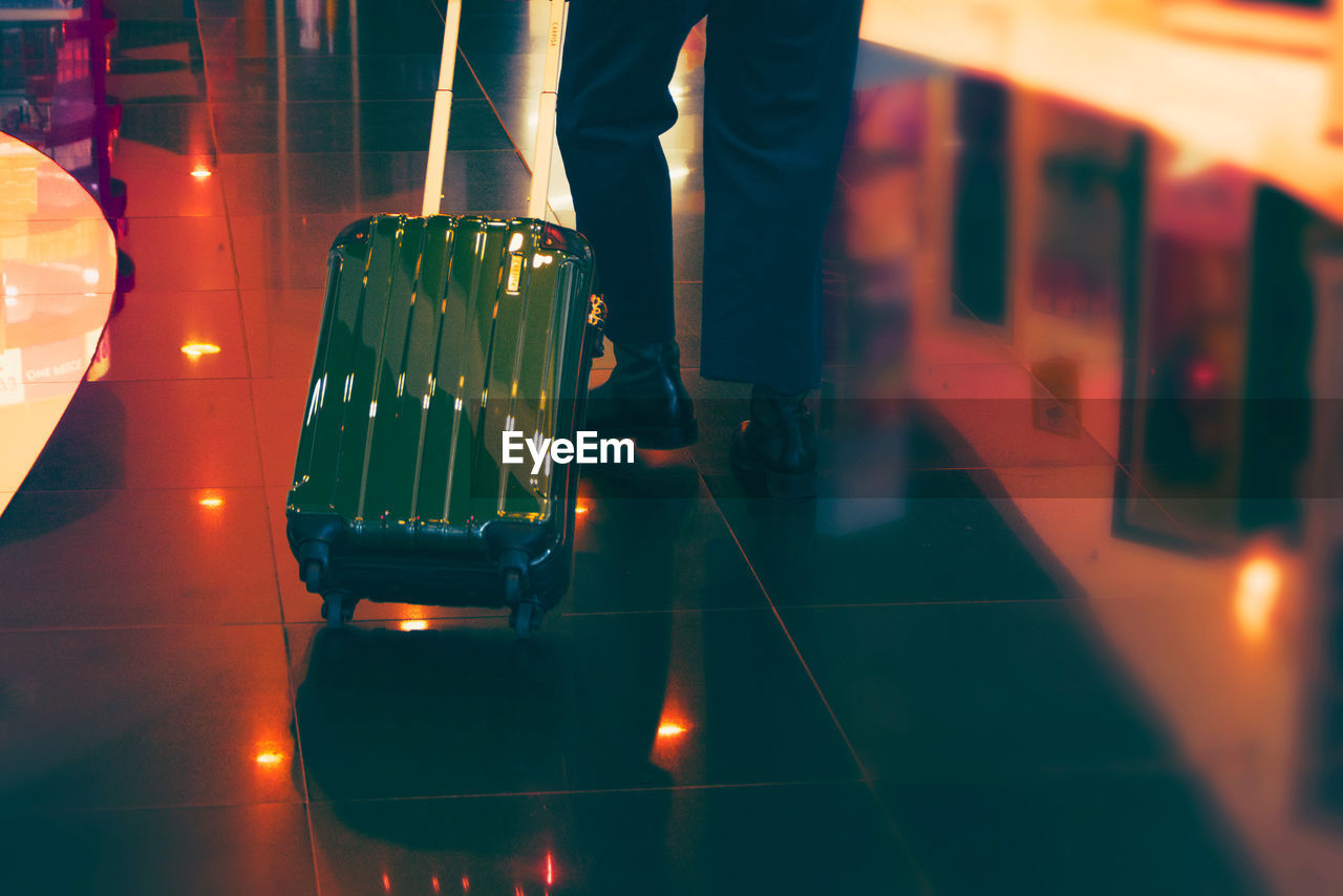 Low section of man with wheeled luggage on tiled floor