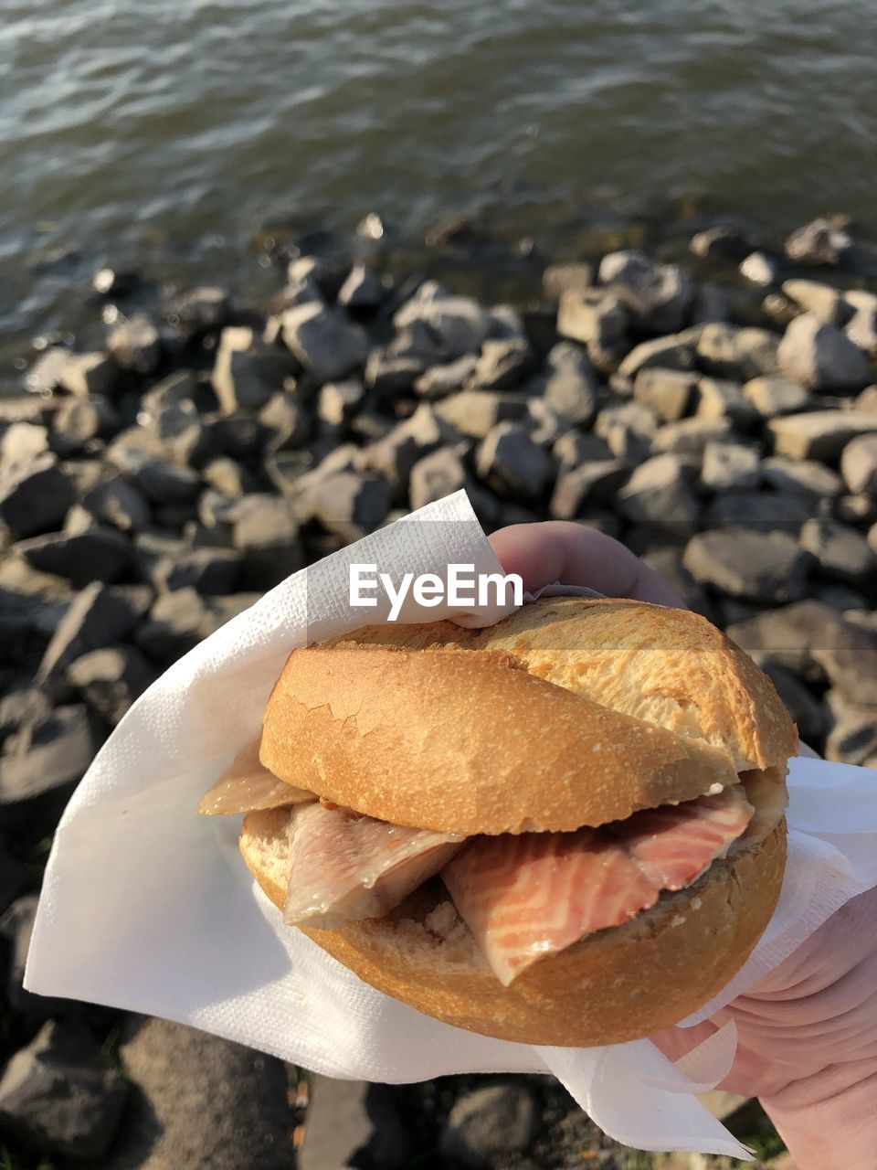 Cropped hand holding burger at beach