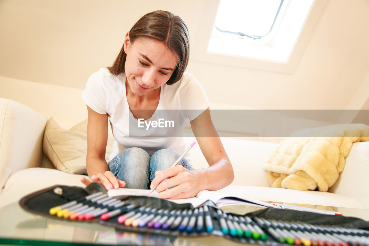 Young woman drawing while sitting on sofa at home