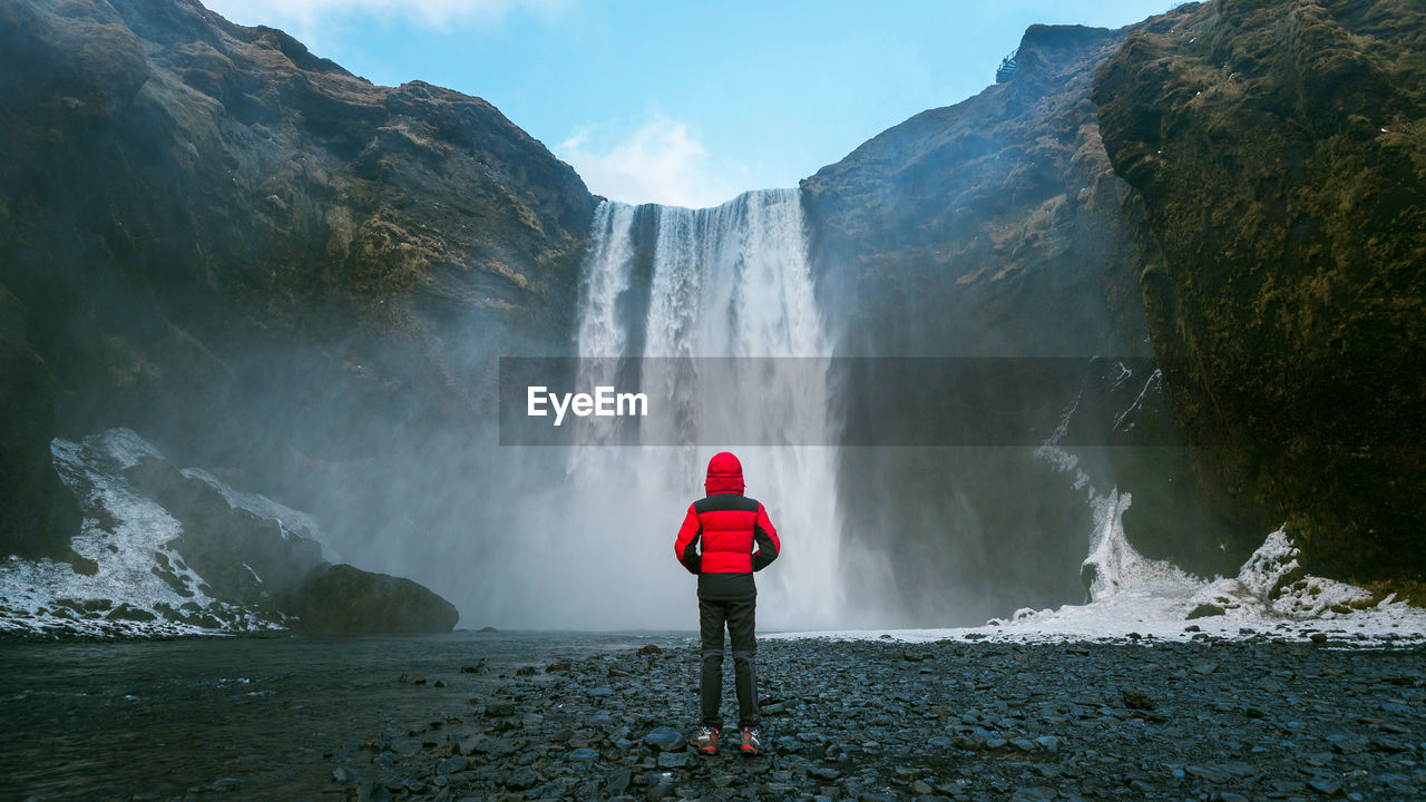 Rear view of man standing by skogafoss