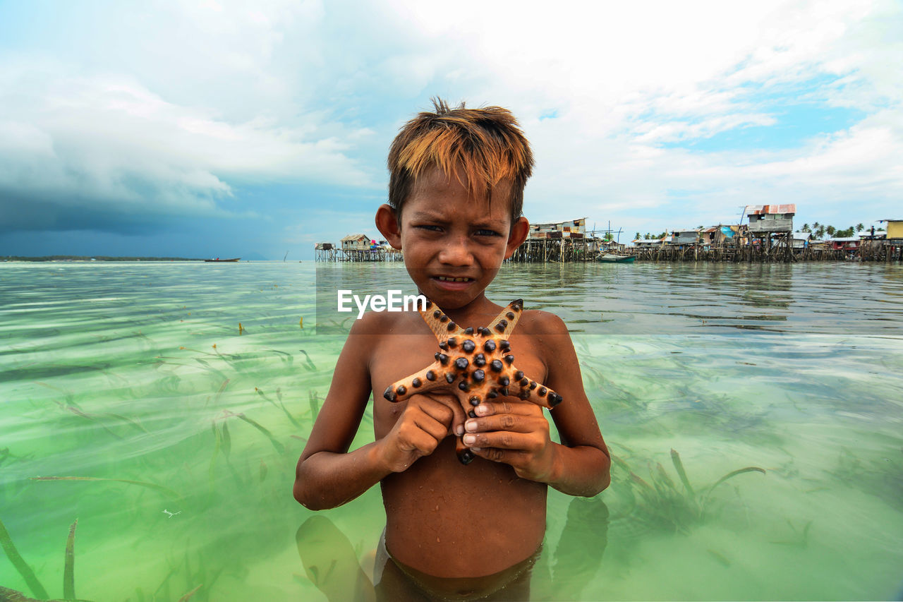 PORTRAIT OF BOY STANDING AGAINST SEA