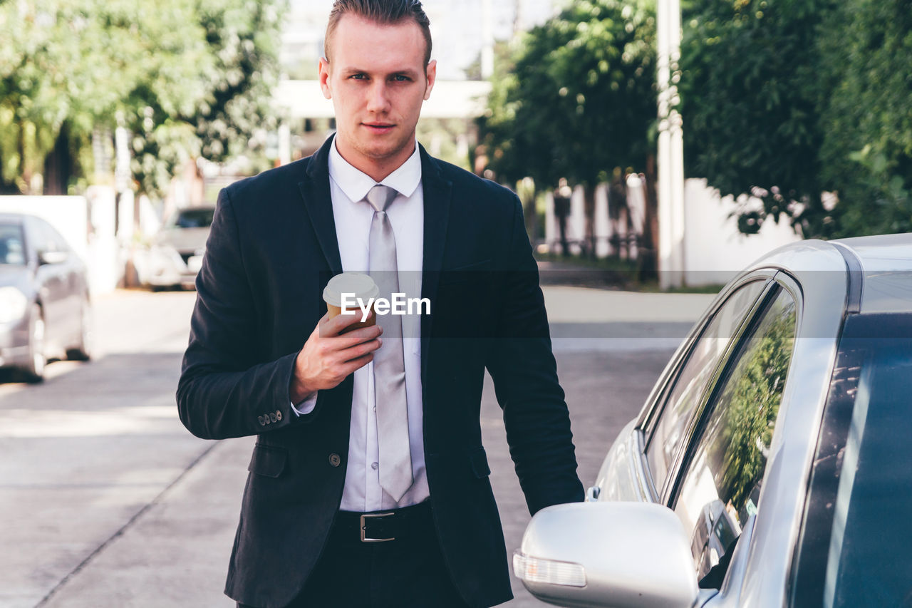 Portrait of businessman standing with car on road