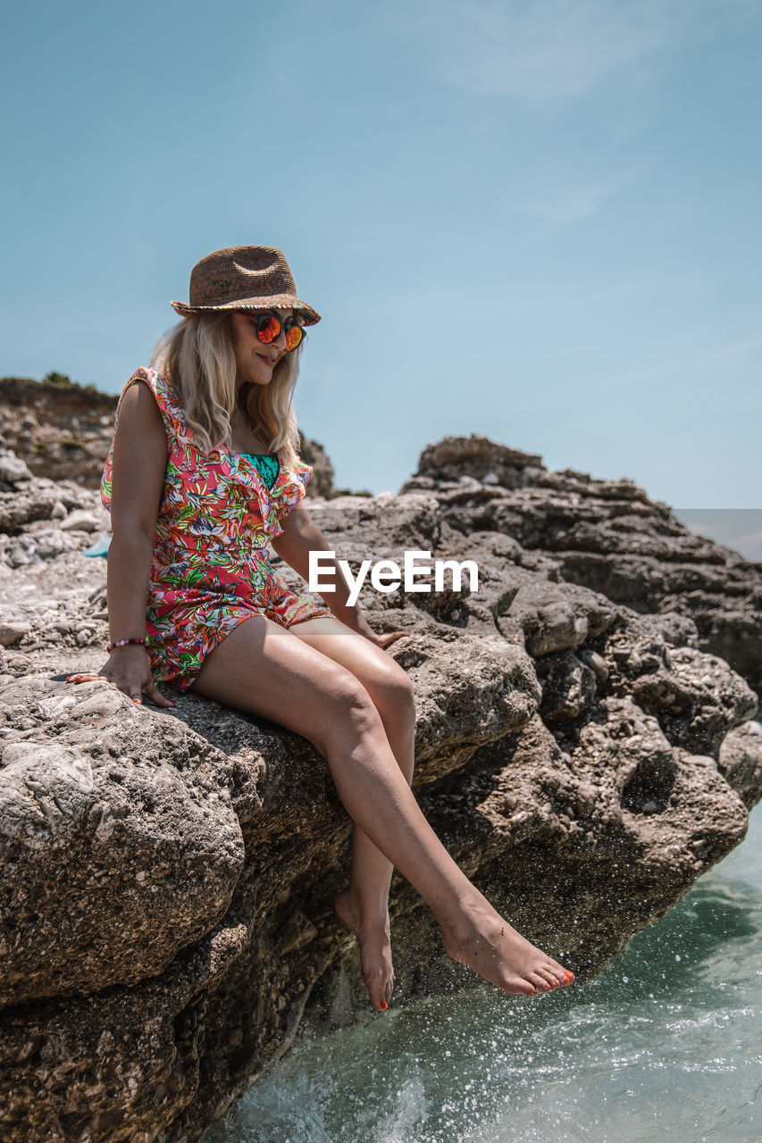 Young woman standing on rock by sea against sky