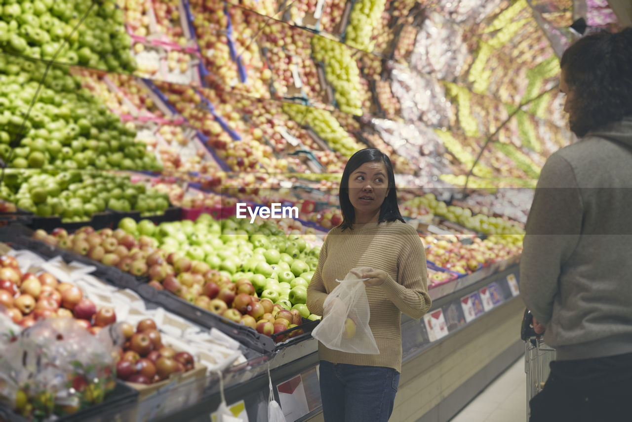 View of couple standing in supermarkets and talking while choosing apples