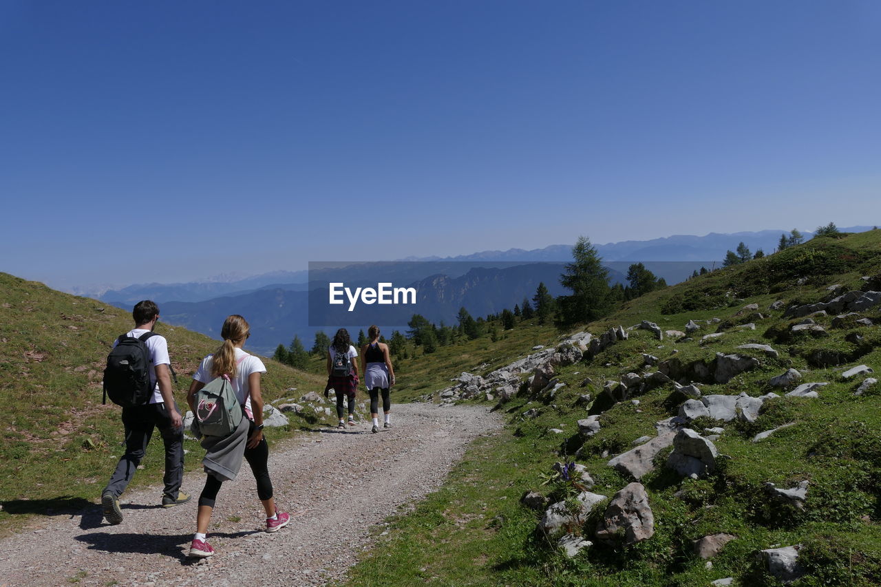 PEOPLE WALKING ON MOUNTAIN AGAINST CLEAR SKY