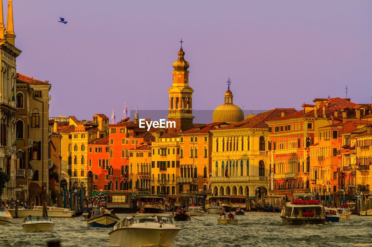 Boats in canal amidst buildings against sky during sunset