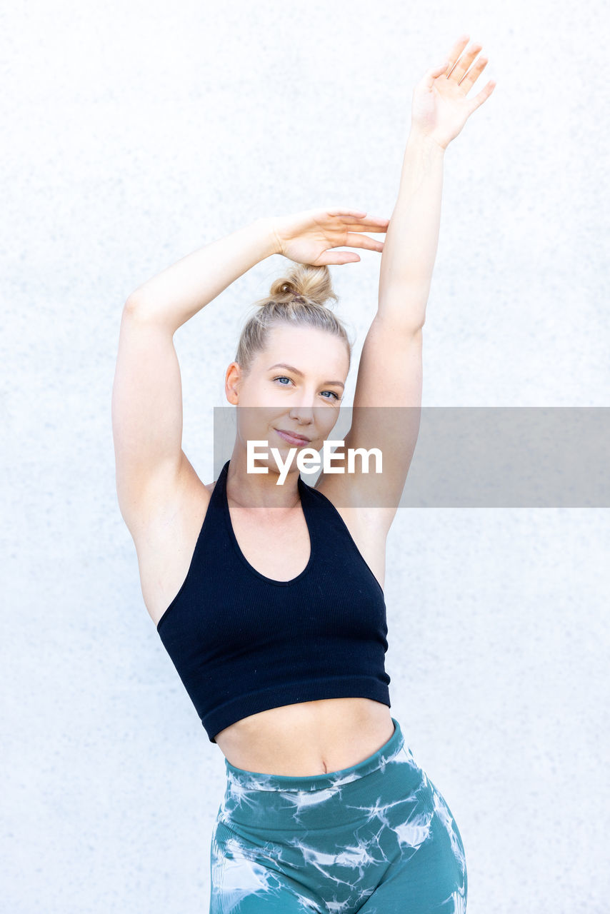 portrait of young woman with arms raised standing against white background