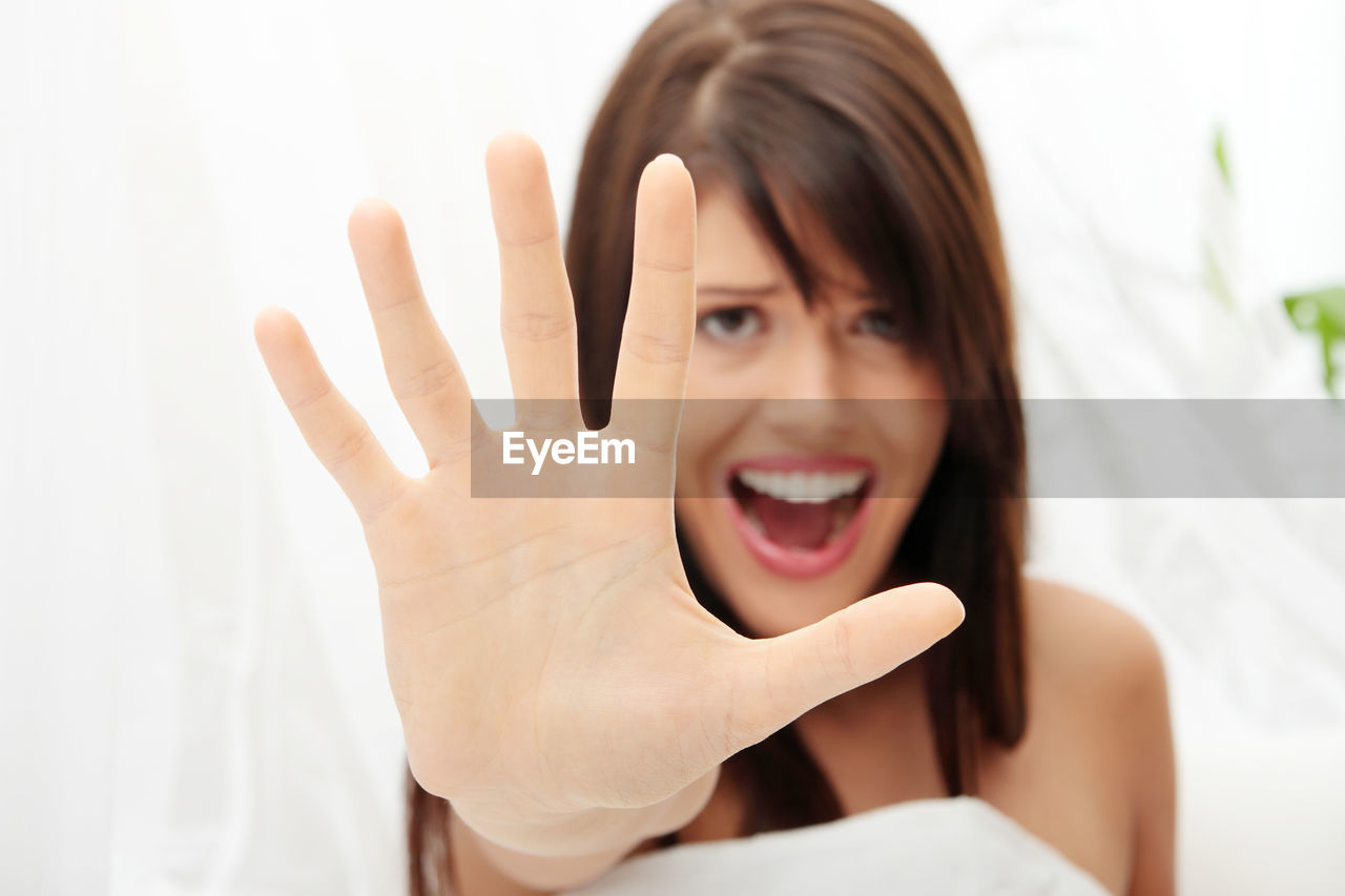 Portrait of scared woman screaming while showing stop gesture at home