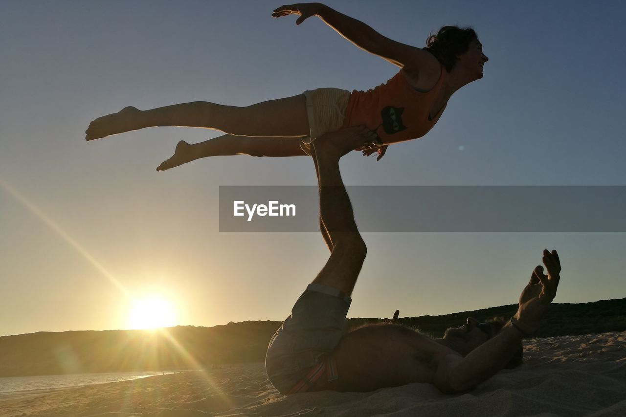Man lifting woman on feet on shore at beach during sunset