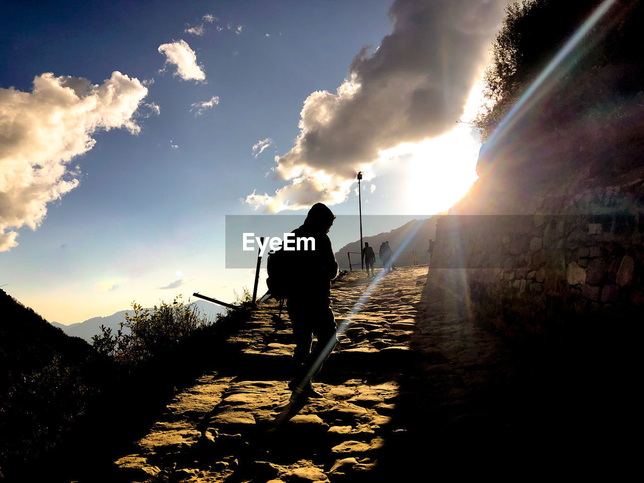 REAR VIEW OF SILHOUETTE MAN WALKING AGAINST BRIGHT SKY