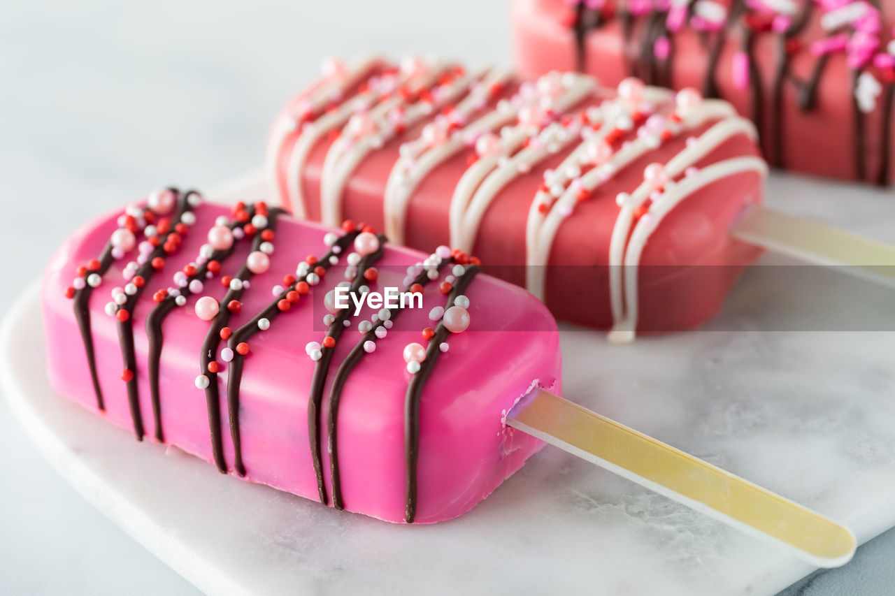 A close up of homemade cakesicles for valentine's day on a marble slab.