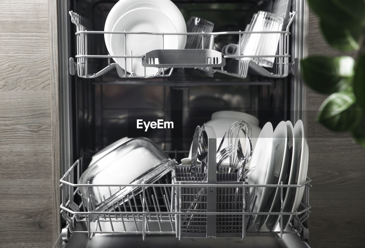 Front view of open automatic stainless steel built-in dishwasher machine with clean utensils