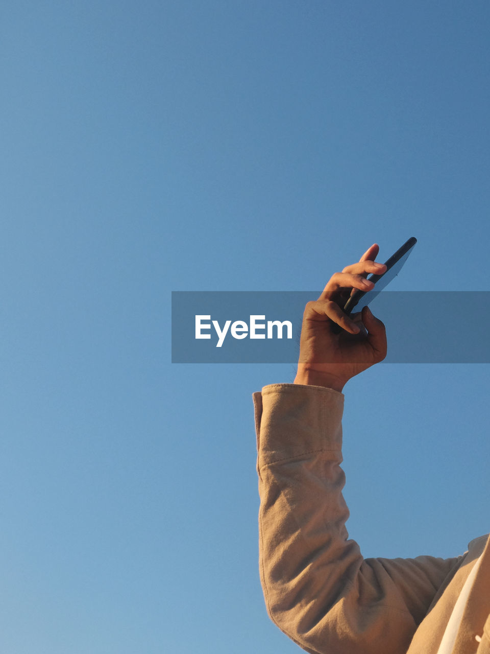 LOW ANGLE VIEW OF HAND HOLDING MOBILE PHONE AGAINST CLEAR SKY