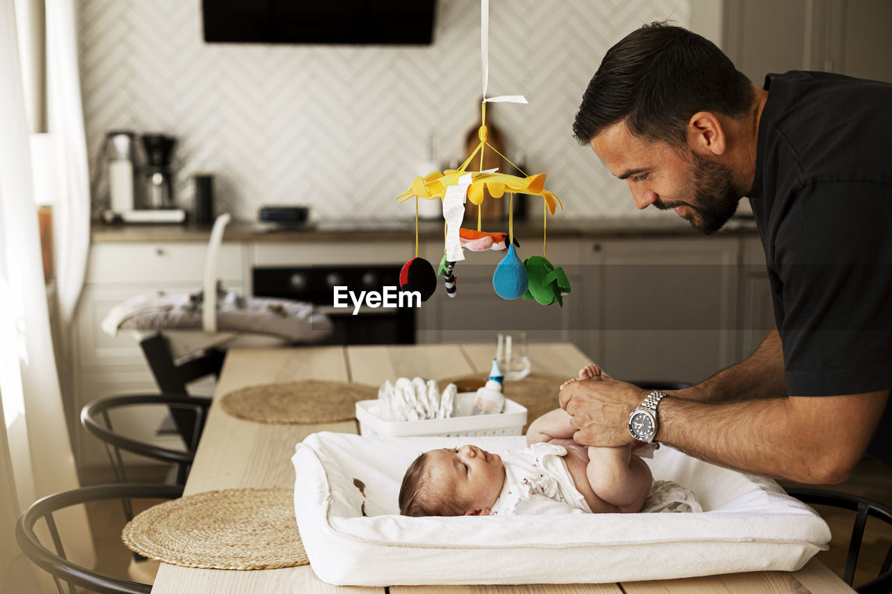 Father changing diaper of son lying down on table at home