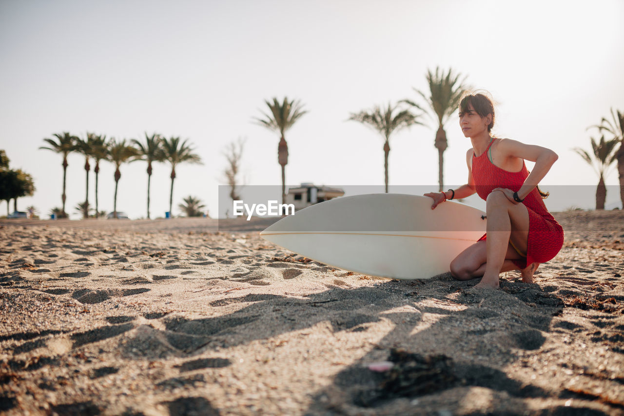 Full length of young woman on palm trees at beach against sky