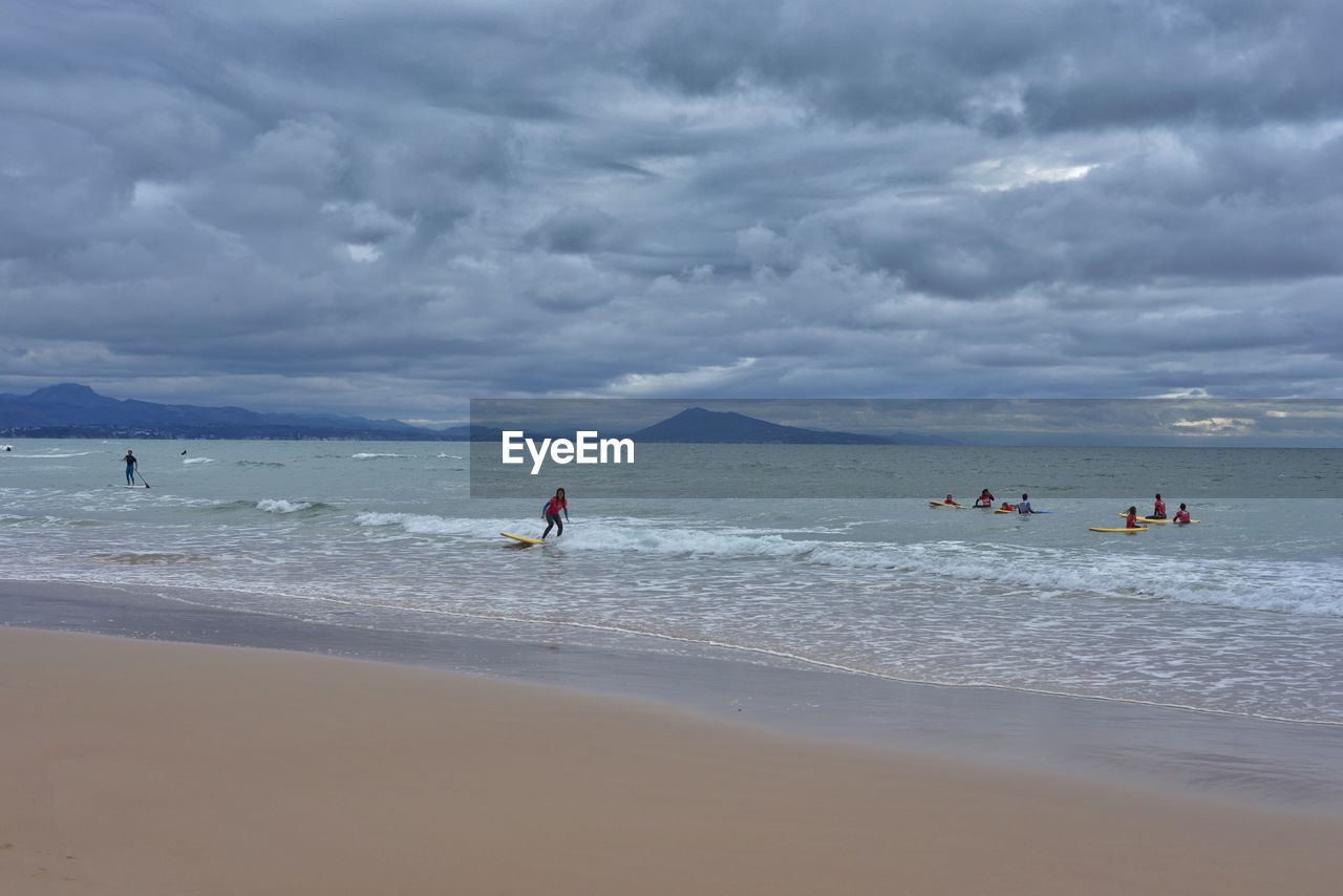 People surfing in sea against cloudy sky