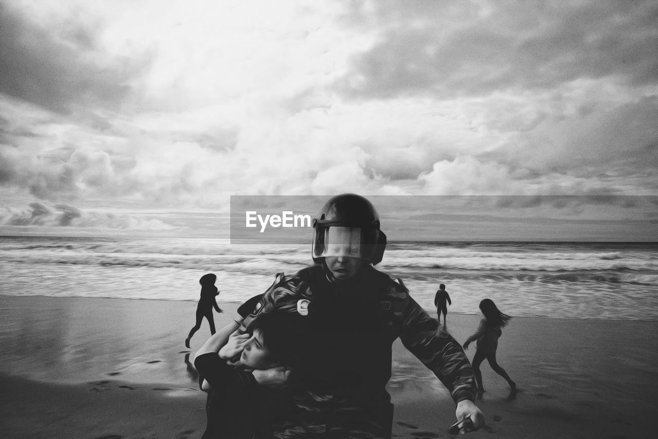 BOYS STANDING ON BEACH AGAINST SKY