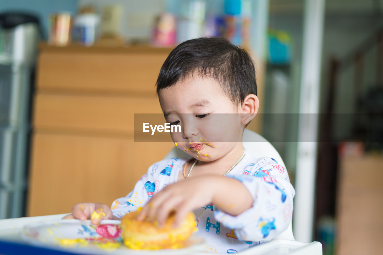 Innocent boy having food while sitting on high chair at home