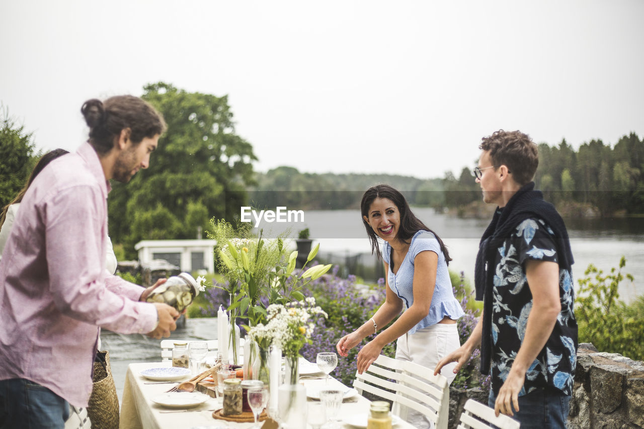 Happy multi-ethnic friends setting table for dinner party in backyard against clear sky