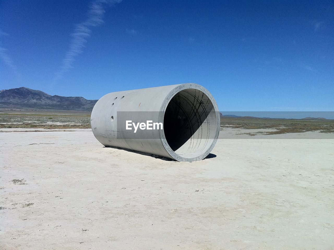 Concrete pipe on field against blue sky