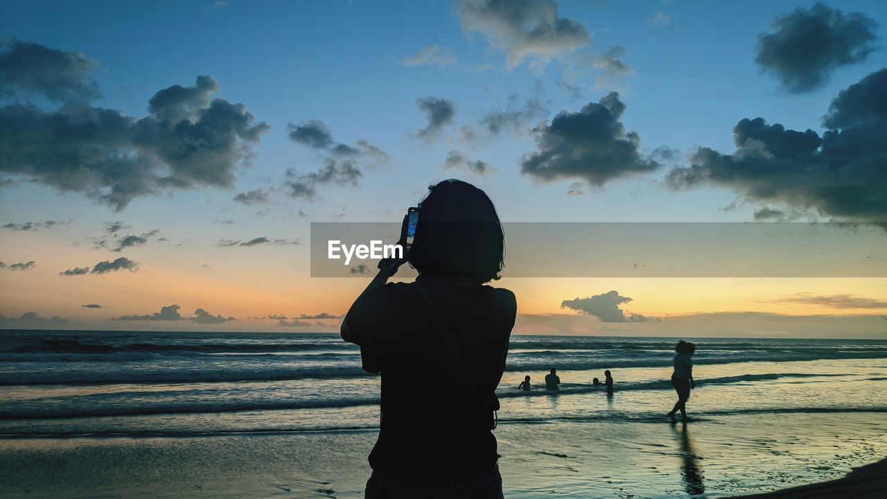 Silhouette woman standing on beach against sky during sunset