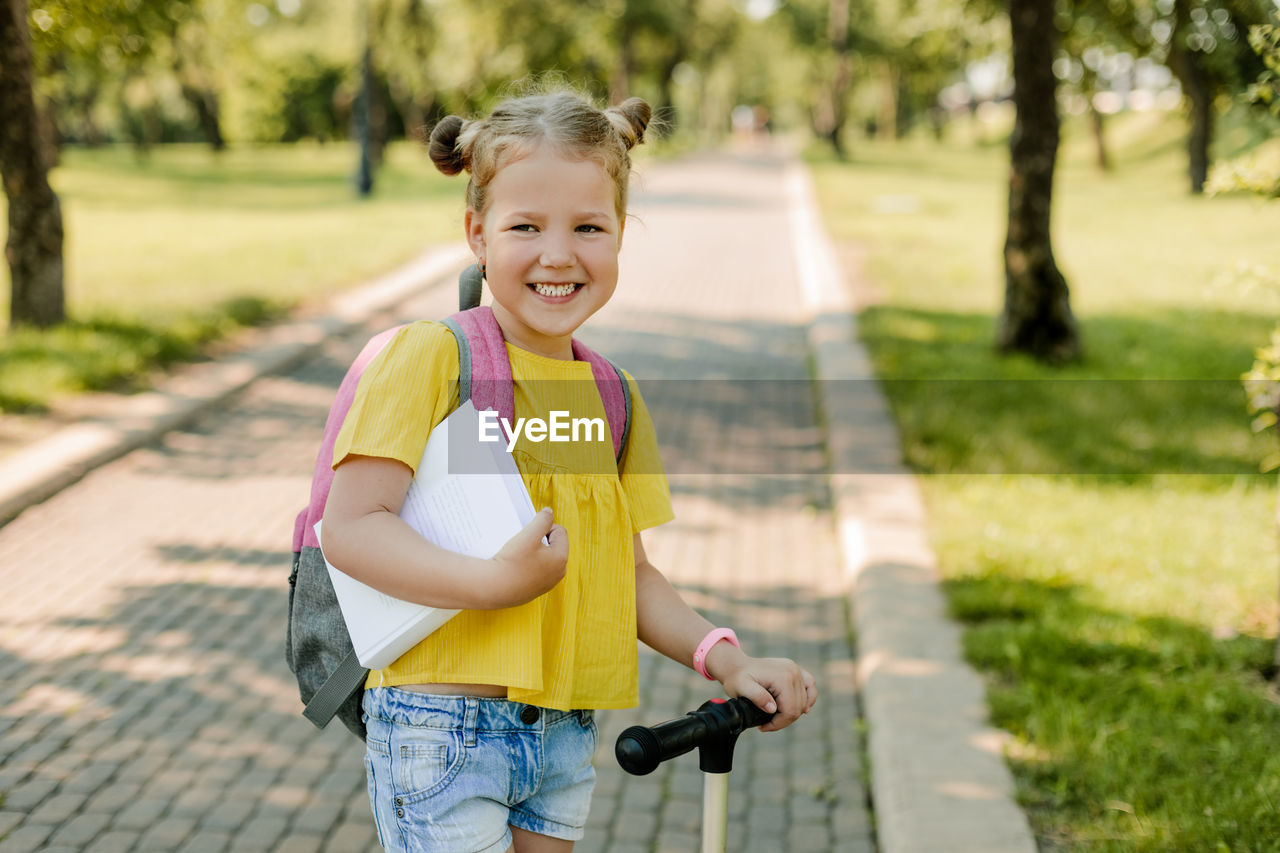 A beautiful little girl rides a scooter on her way back to school