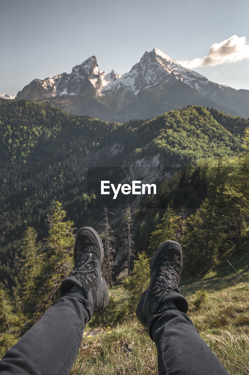 Low section of man sitting over mountain against sky