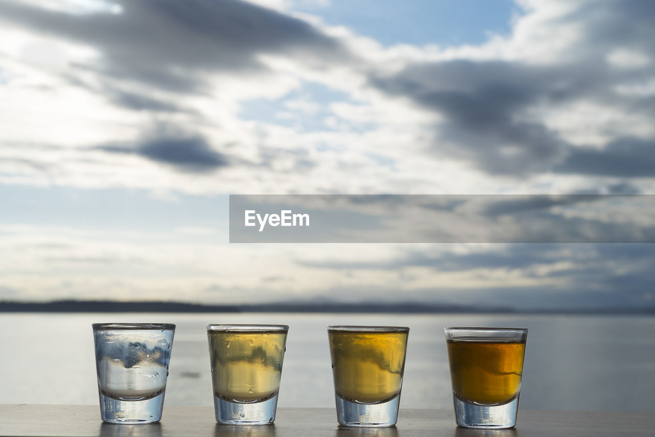 Tequila shots on table by sea against sky