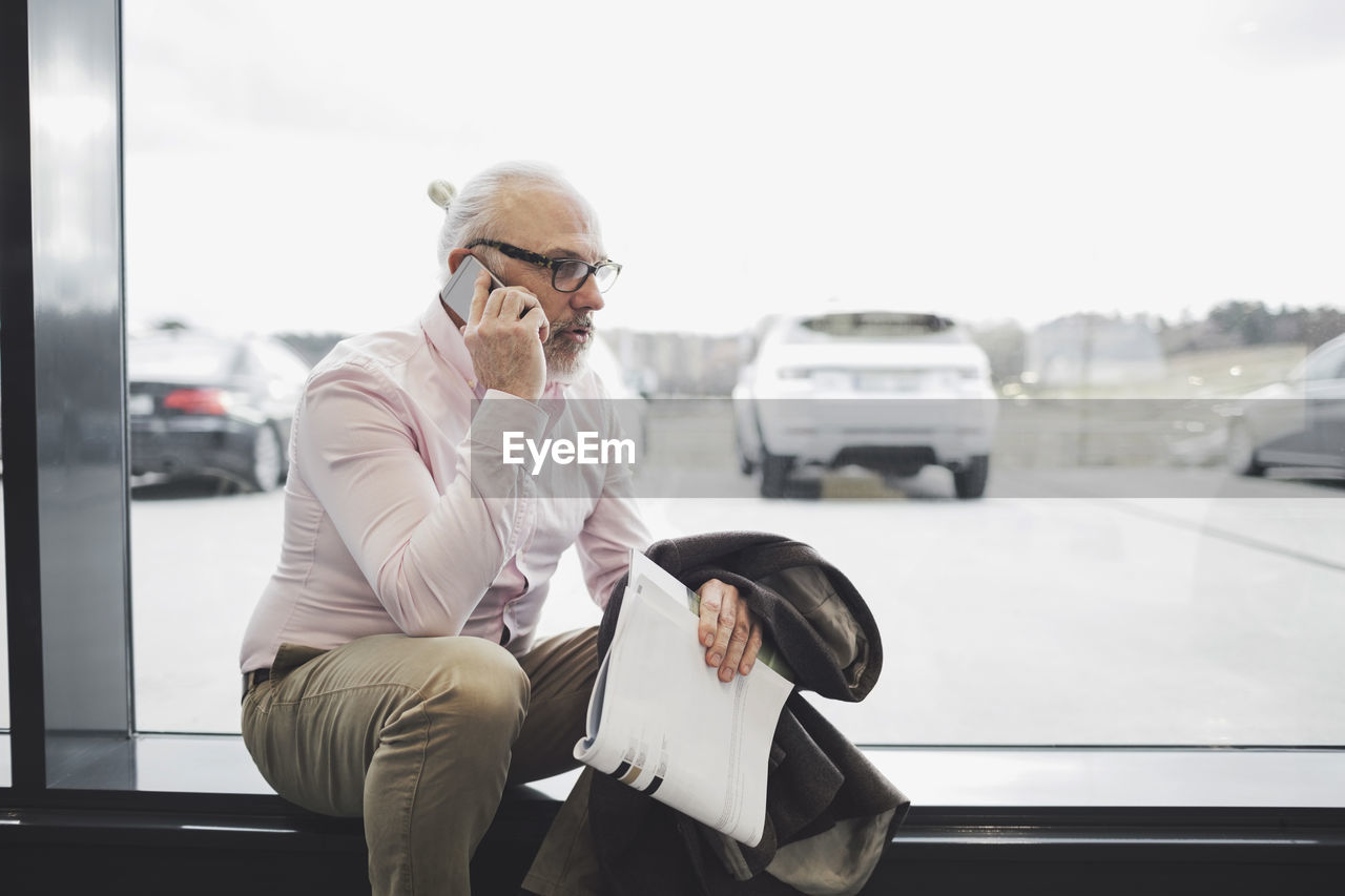 Man talking on phone while sitting by glass window at car showroom