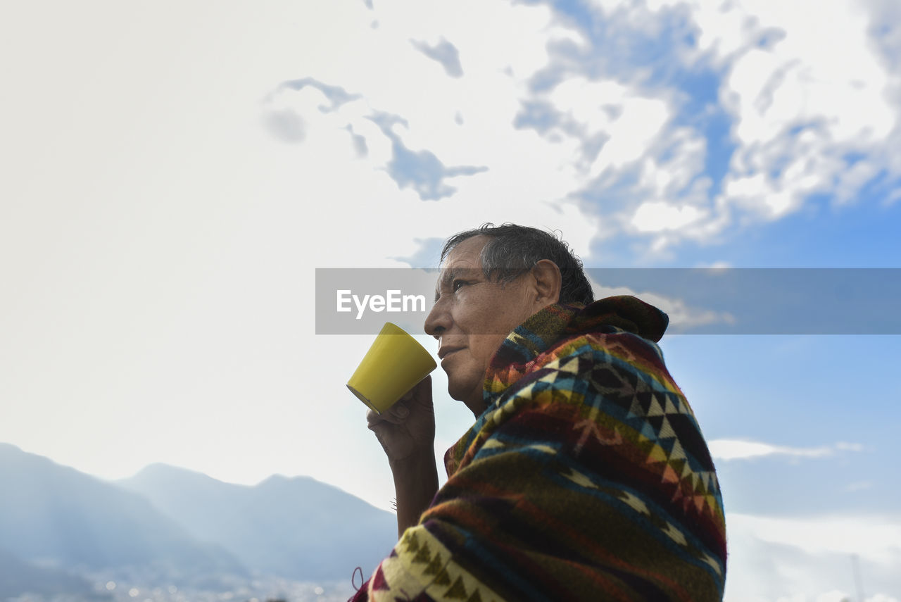 Man wearing traditional poncho looking away while drinking coffee