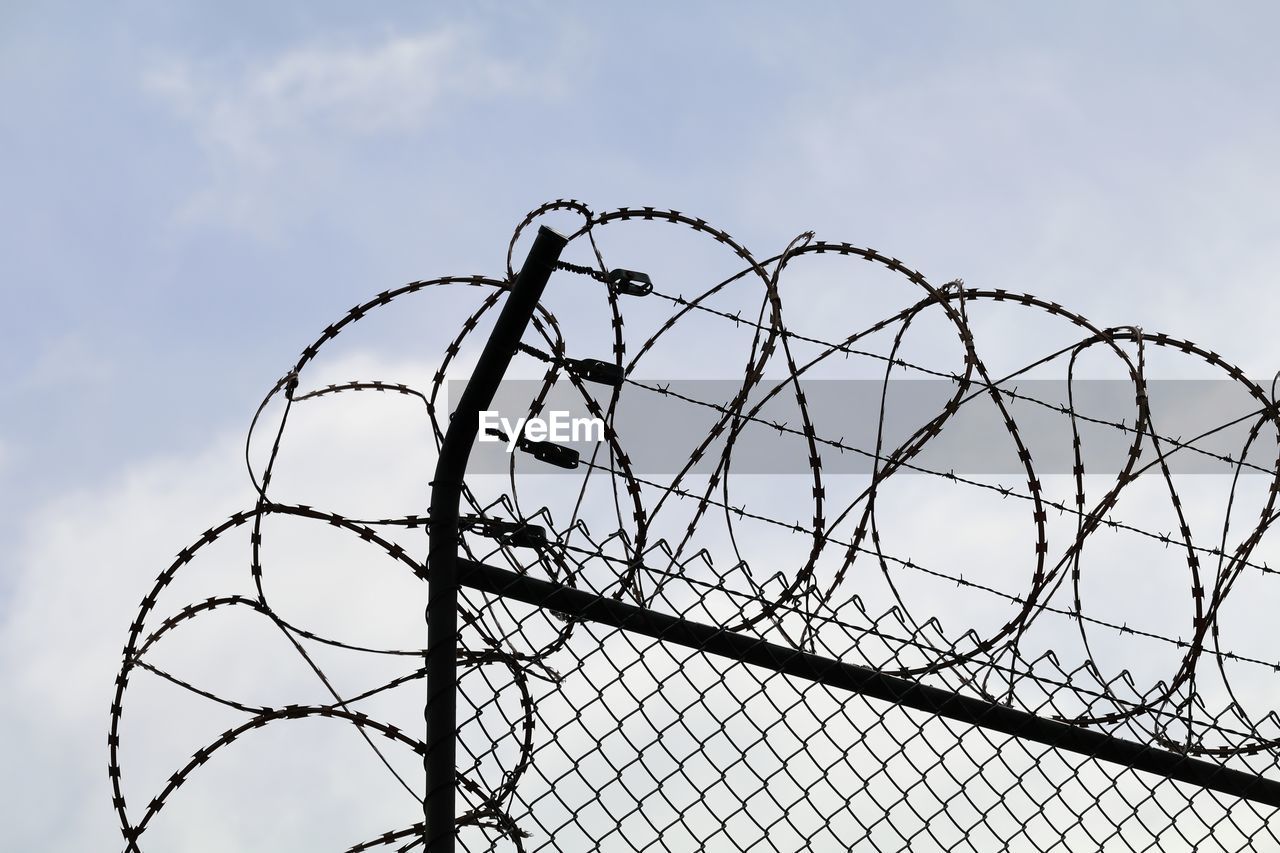 Low angle view of razor wire over chainlink fence against sky