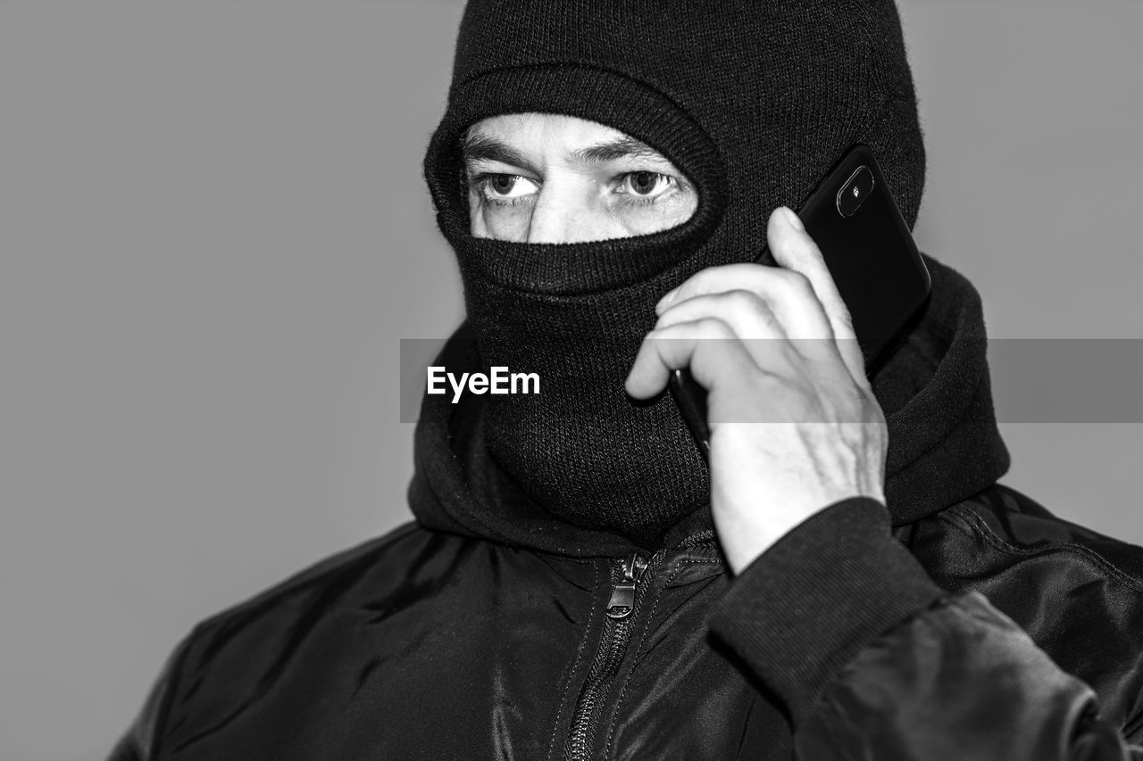 black, portrait, clothing, one person, adult, studio shot, headshot, disguise, cap, black and white, monochrome, human face, mask, looking at camera, monochrome photography, young adult, facial hair, men, obscured face, mask - disguise, hiding, protective mask - workwear, headgear, covering, indoors, hood, hood - clothing, human head, hat, person, protection