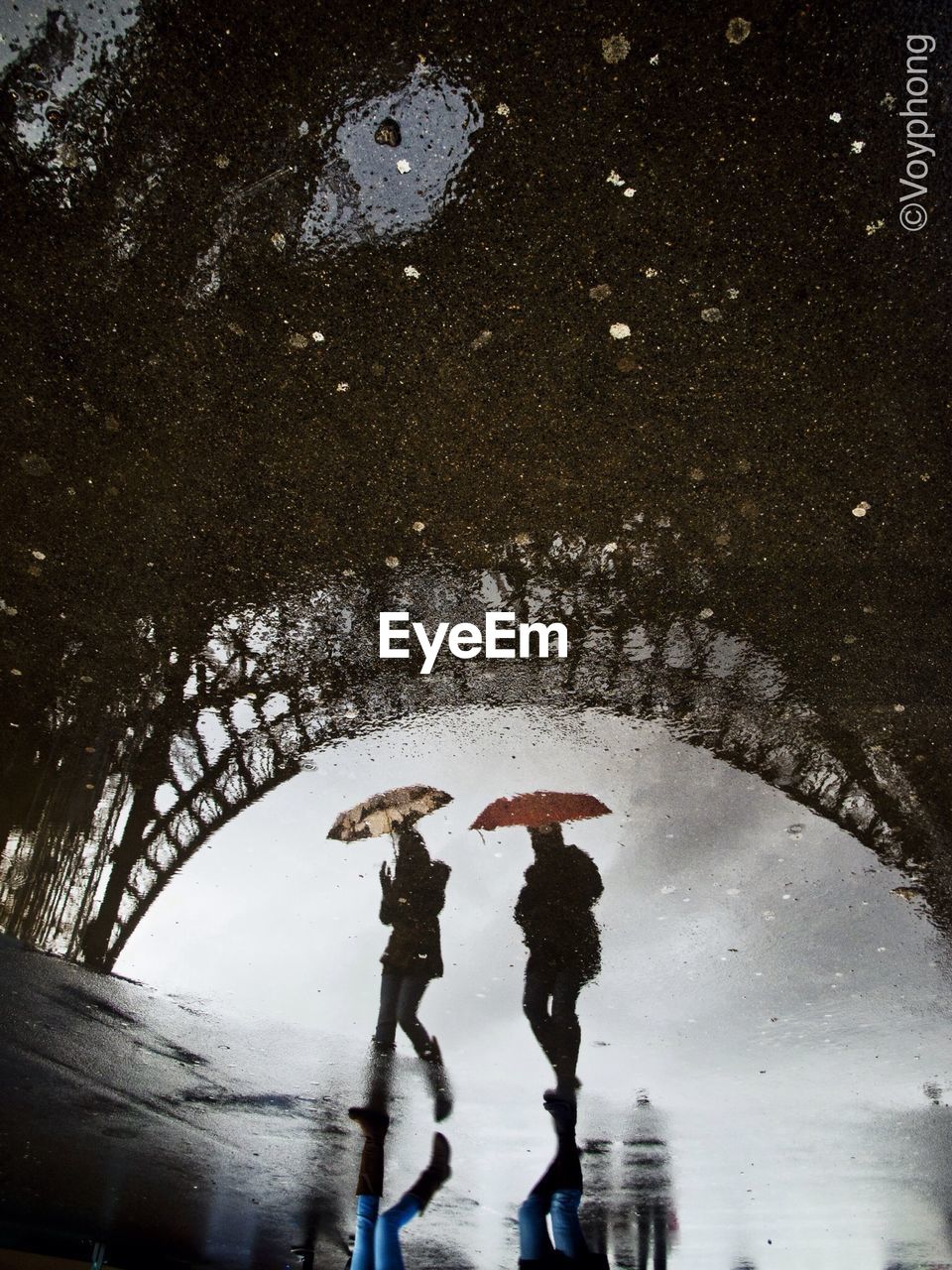 Reflection of eiffel tower and two people in puddle water