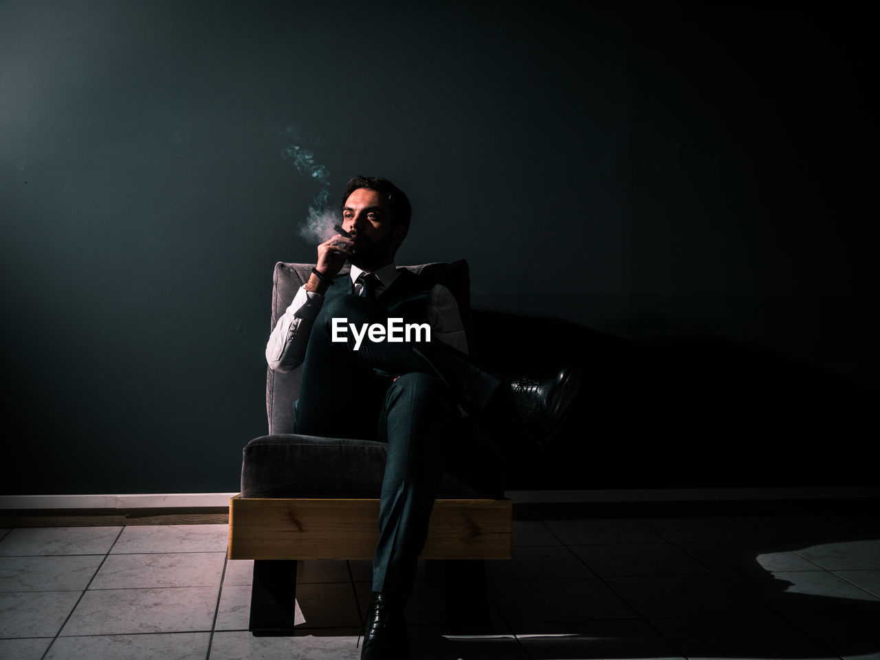 Man smoking cigar while sitting on chair at night