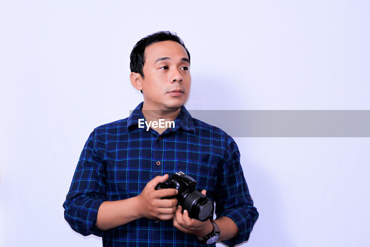 Man with camera looking away while standing against white background