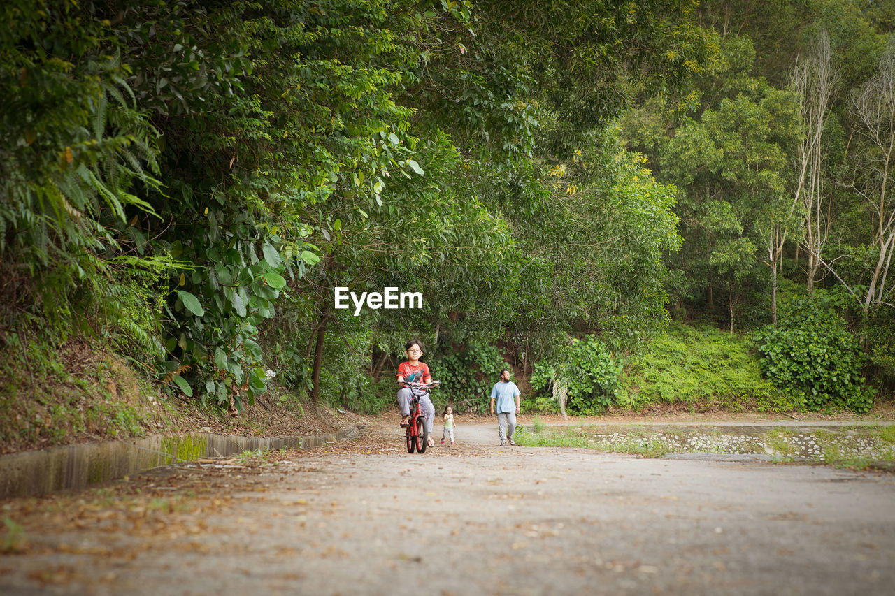 Girl riding bicycle on road against trees in park