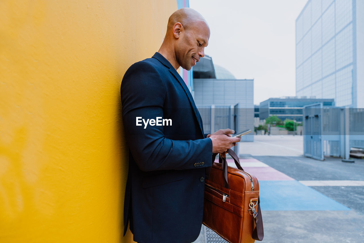 side view of young man with suitcase while standing against yellow wall