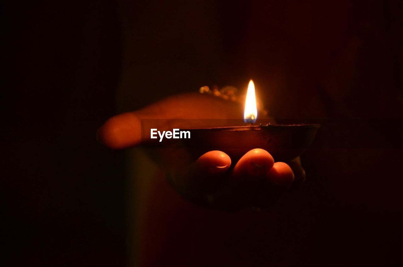 Close-up of hand holding lit diya in dark room