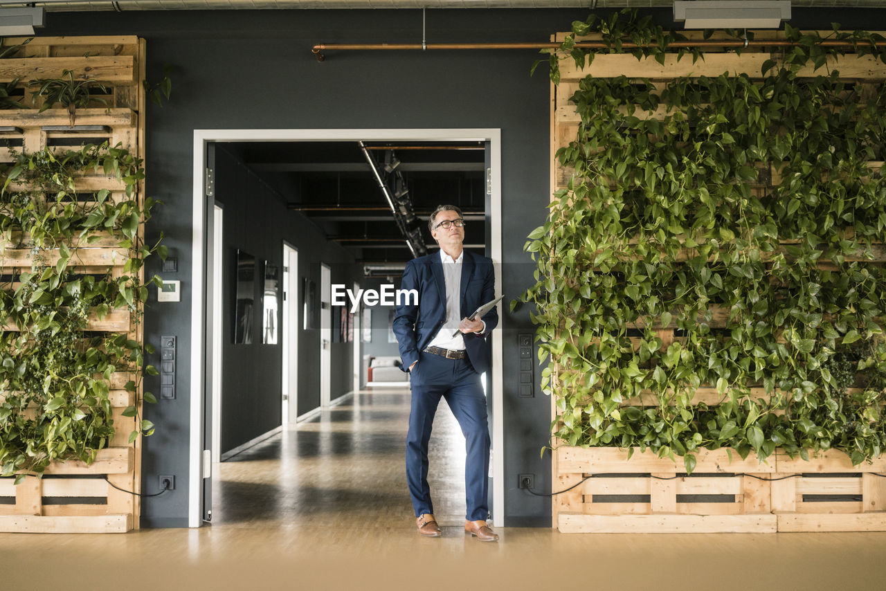 Mature businessman with laptop standing in green office