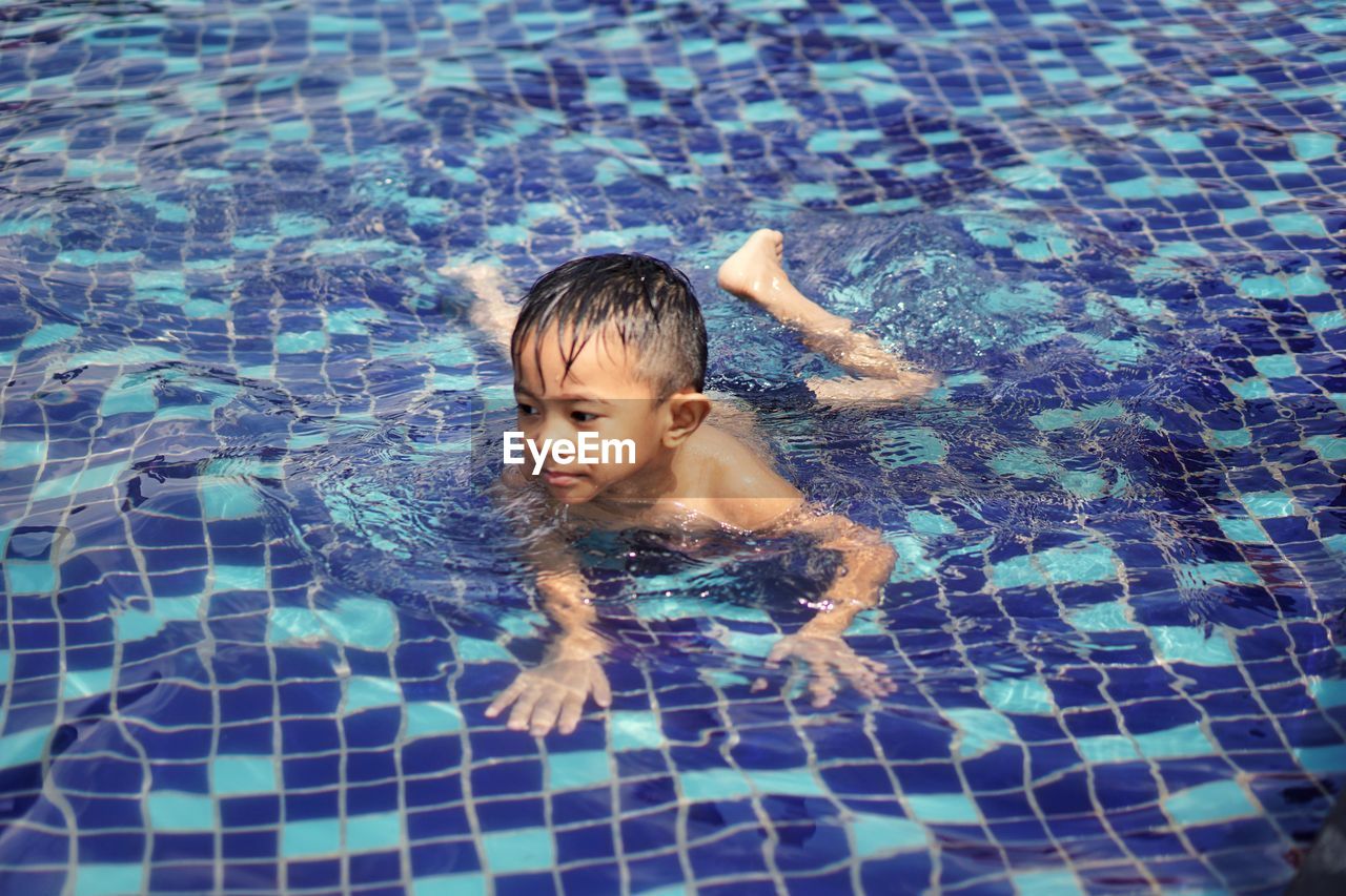 High angle view of shirtless boy swimming in pool